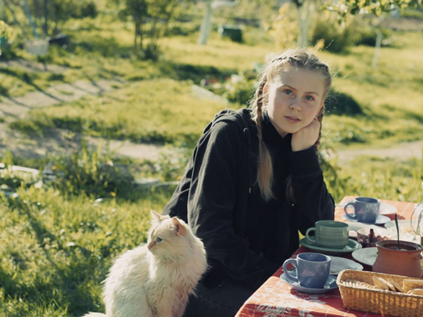 Image from film of girl sitting at picnic table with a cat. Links to event page