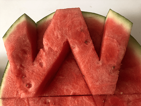 Photo of a watermelon, halved, with the letter W sculpted out in relief.